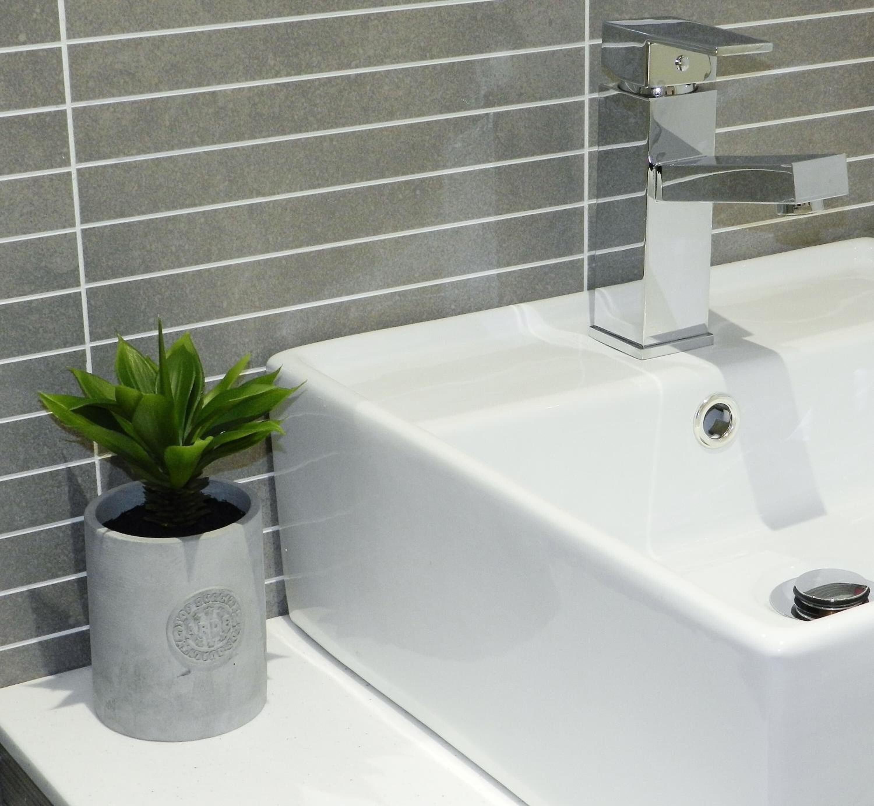 A modern bathroom with a white bathtub, a chrome faucet, and a potted plant on the side.