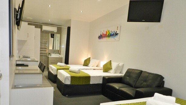 A hotel room with two beds, a sofa, a TV, and a bathroom visible through an open door. - Copper City Motel (Pioneer)