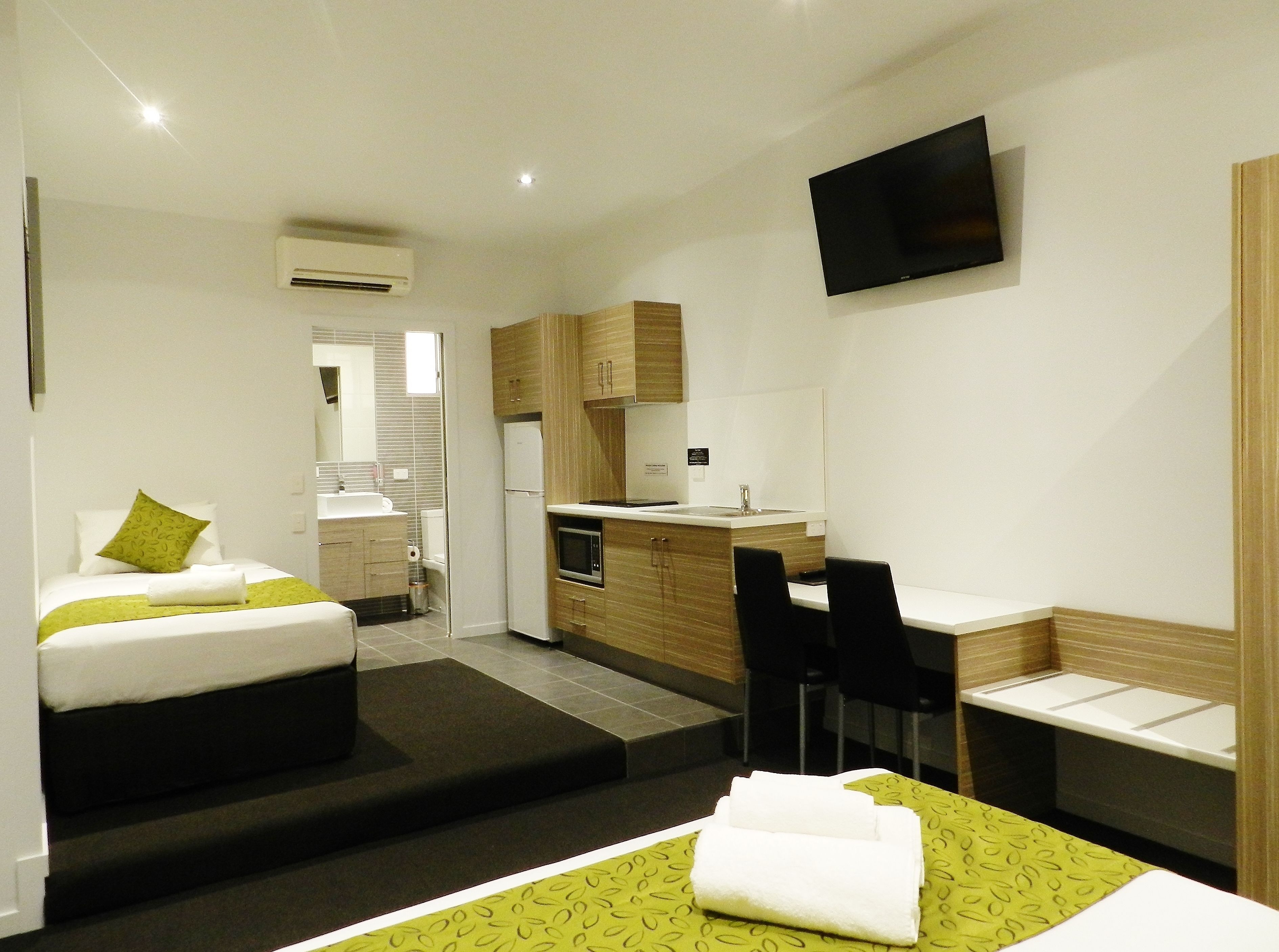 A hotel room with a bed, a desk, a chair, a TV, and a kitchenette.