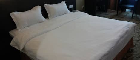 A hotel room with a large bed, a desk with a lamp, and a chair.