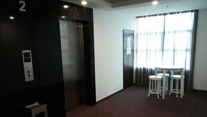 A hotel room with a private elevator, a small trash bin, a table with four chairs, and a window with curtains. - Eminent Hotel (Kota Kinabalu)