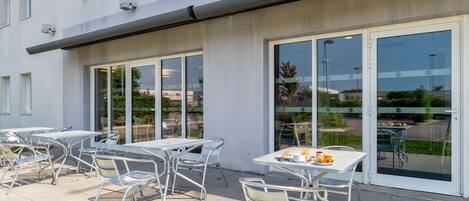 An outdoor patio with tables and chairs, large windows, and a building facade.