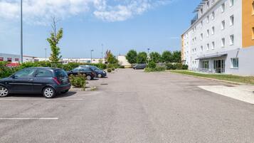 Un parking avec plusieurs voitures, un bâtiment doté de nombreuses fenêtres et un ciel dégagé.