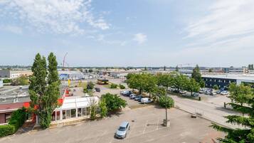 Un parking avec quelques voitures, des arbres et des bâtiments en arrière-plan.