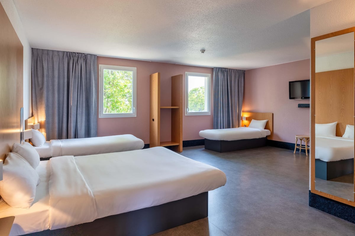 Una habitación de hotel con dos camas, televisión, espejo y ventana con cortinas.