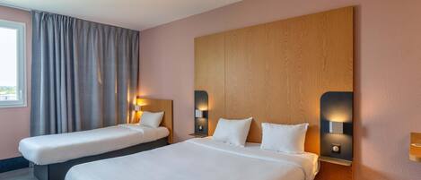A hotel room with two beds, a large wooden headboard, bedside lamps, and a window with curtains.
