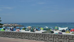 A beach with multiple colorful tents and umbrellas, a stone wall in the foreground, and the ocean in the background. - Grampus Resort Shirahama (Shirahama)