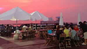 An outdoor dining area with tables and chairs, umbrellas, and a view of the city skyline at sunset. - Grampus Resort Shirahama (Shirahama)