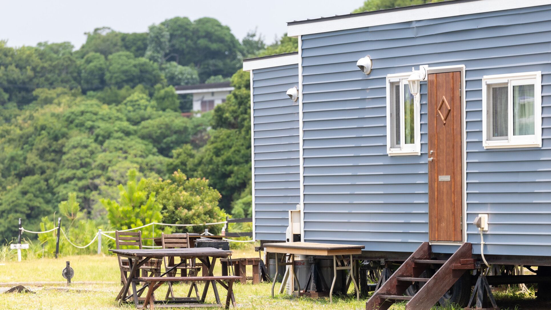 Une maison mobile bleue, avec une porte en bois, un petit porche et une table entourée de chaises.