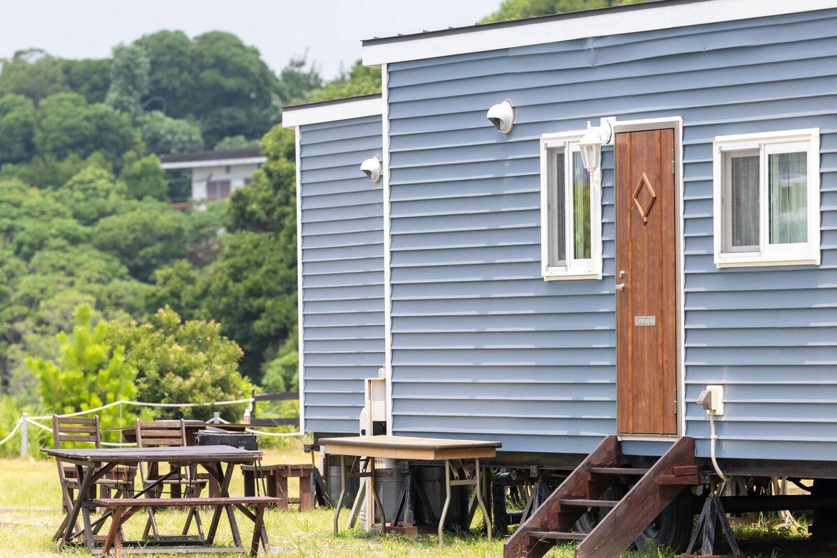 Uma casa móvel azul com porta de madeira, um pequeno alpendre e uma mesa com cadeiras.