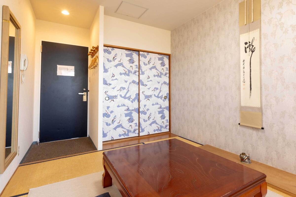 Um quarto com uma mesa de madeira, uma porta preta e um painel deslizante shoji com padrão de grua.