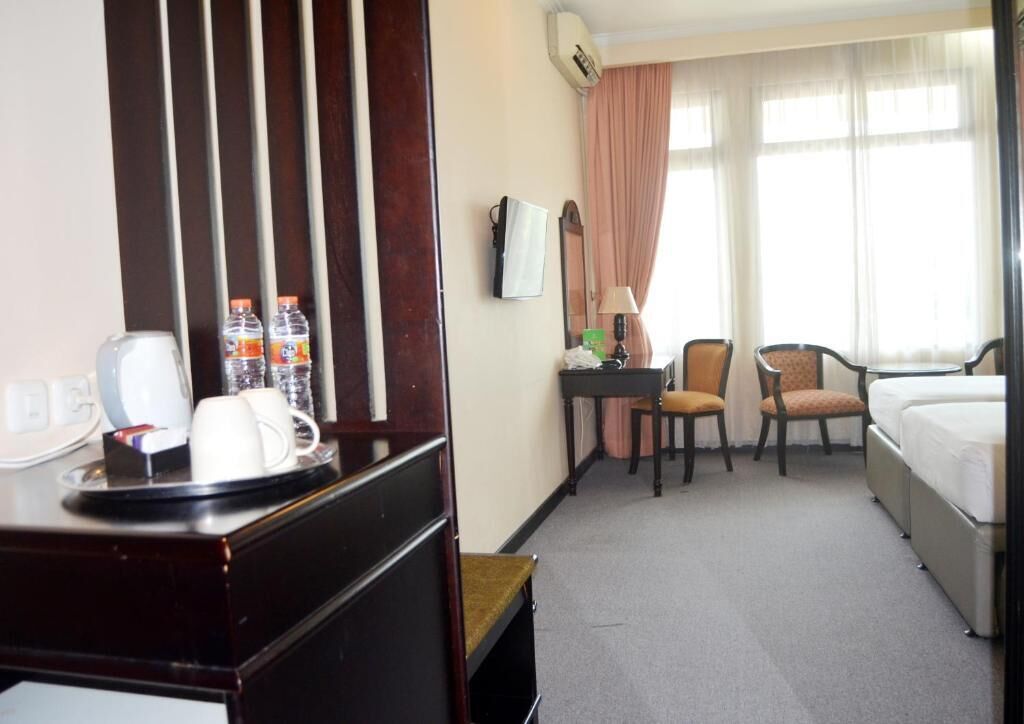 A hotel room with a bed, a desk with a telephone, a chair, a table with a lamp, and a window with curtains.