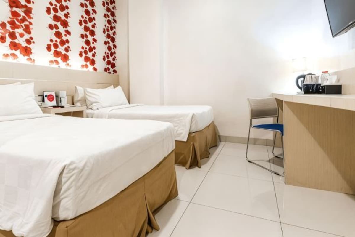 A hotel room with two beds, a desk, a chair, and a TV mounted on the wall.