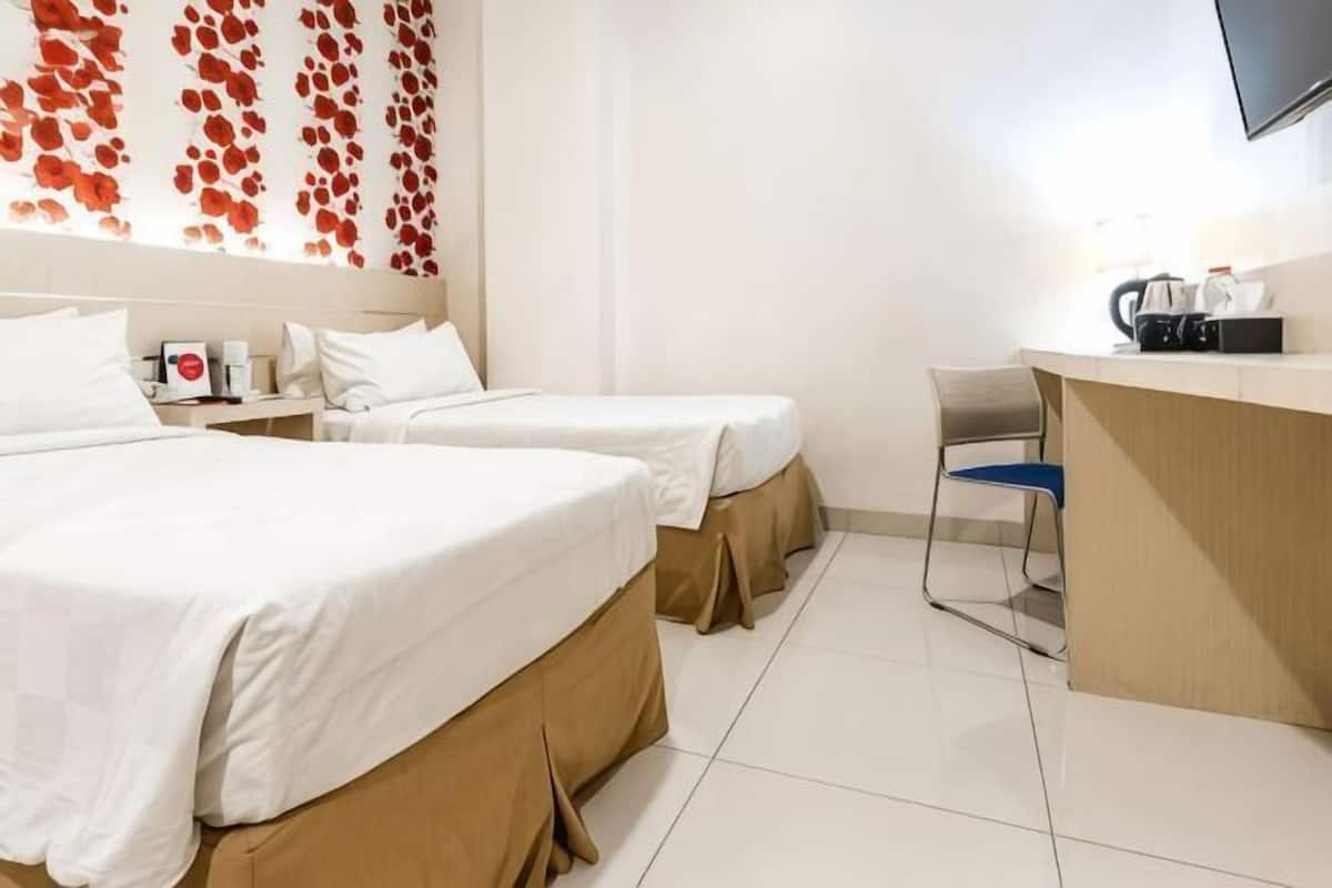 A hotel room with two beds, a desk, a chair, and a TV mounted on the wall.