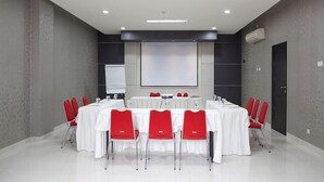 A conference room with a white table, red chairs, a projector screen, and a whiteboard. - Cordela Hotel Medan (Medan)