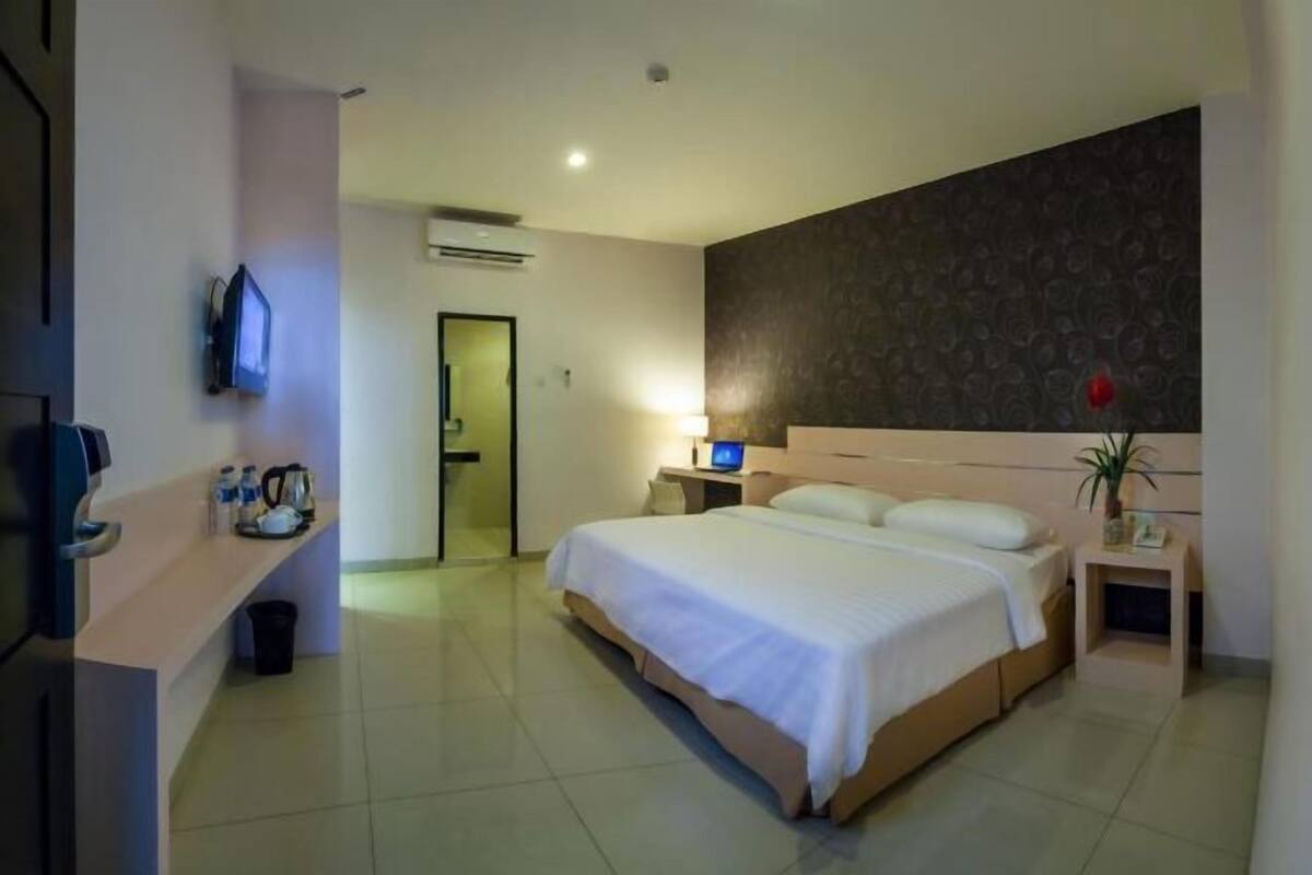 A hotel room with a bed, bedside table, TV, and a small desk with a lamp.