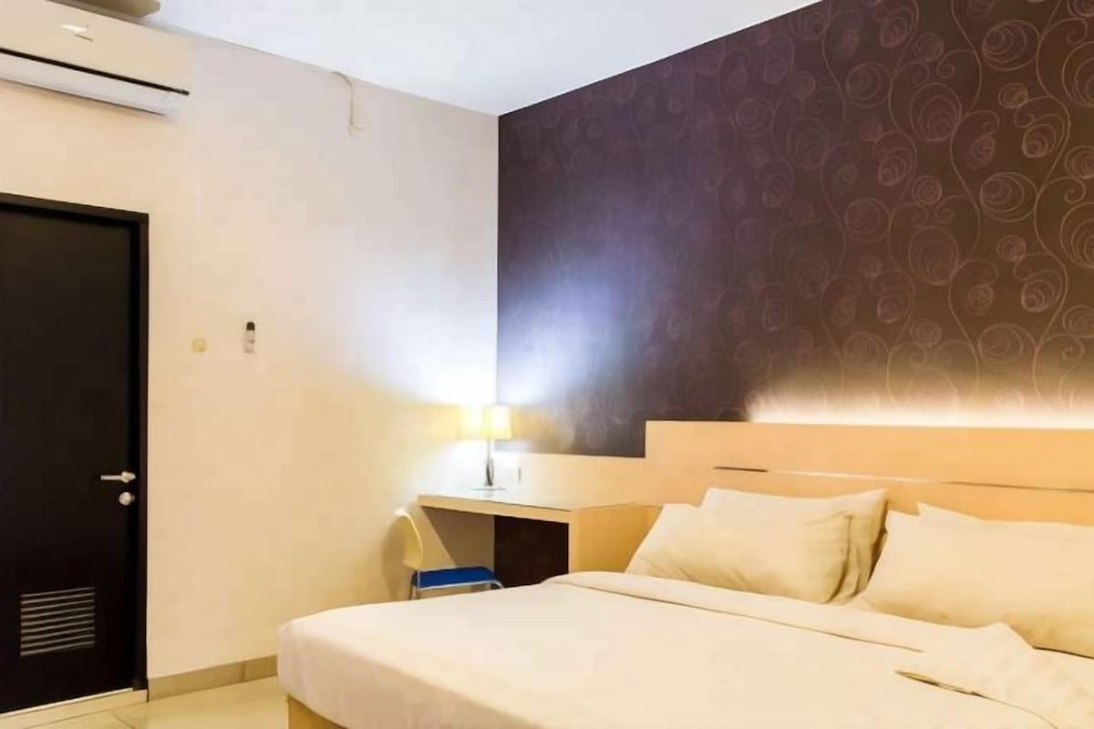 A hotel room with a bed, a desk, a chair, and a wall with a decorative pattern.