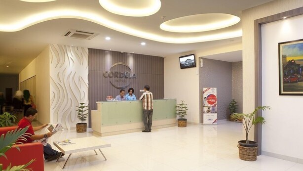 A hotel reception area with a modern design, featuring a reception desk, seating area, and decorative wall panels. - Cordela Hotel Medan (Medan)