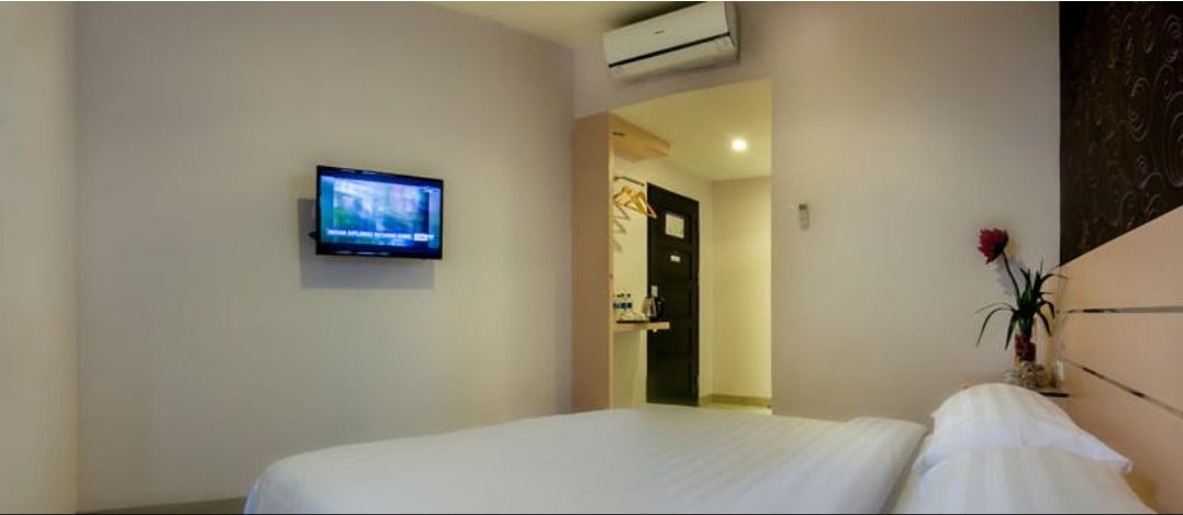 A hotel room with a bed, a television mounted on the wall, and a door leading to a bathroom.
