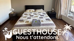 A bedroom with a large bed, two bedside tables, a window with curtains, and two framed pictures on the wall.