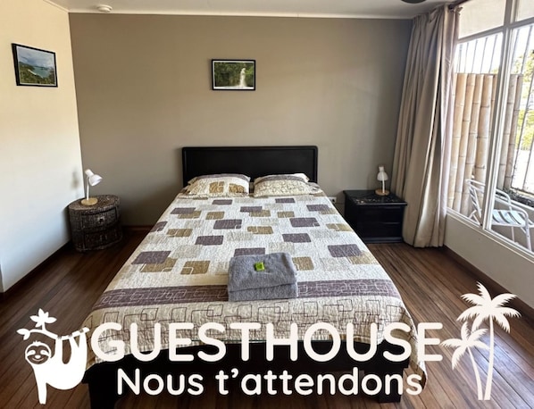 A bedroom with a large bed, two bedside tables, a window with curtains, and two framed pictures on the wall. - Costa Rica Guesthouse (San José)