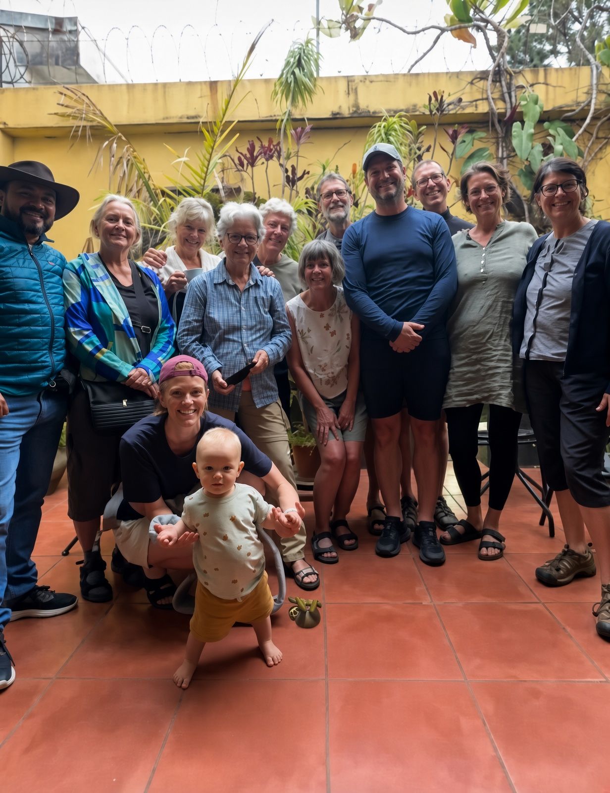 Un grupo de personas reunidas en un patio con baldosas, una pared amarilla y follaje al fondo.