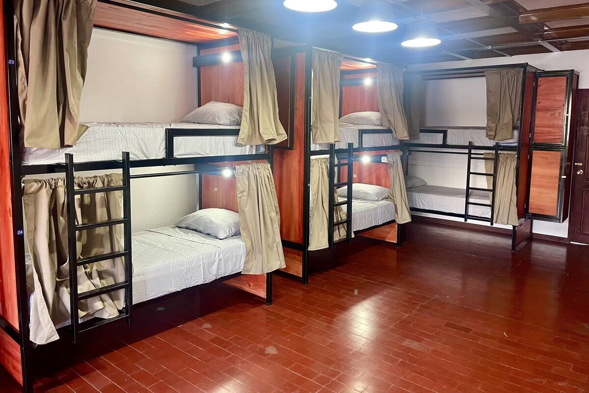 Une chambre de dortoir avec des lits superposés, un plancher en bois et un plafond avec des poutres apparentes.