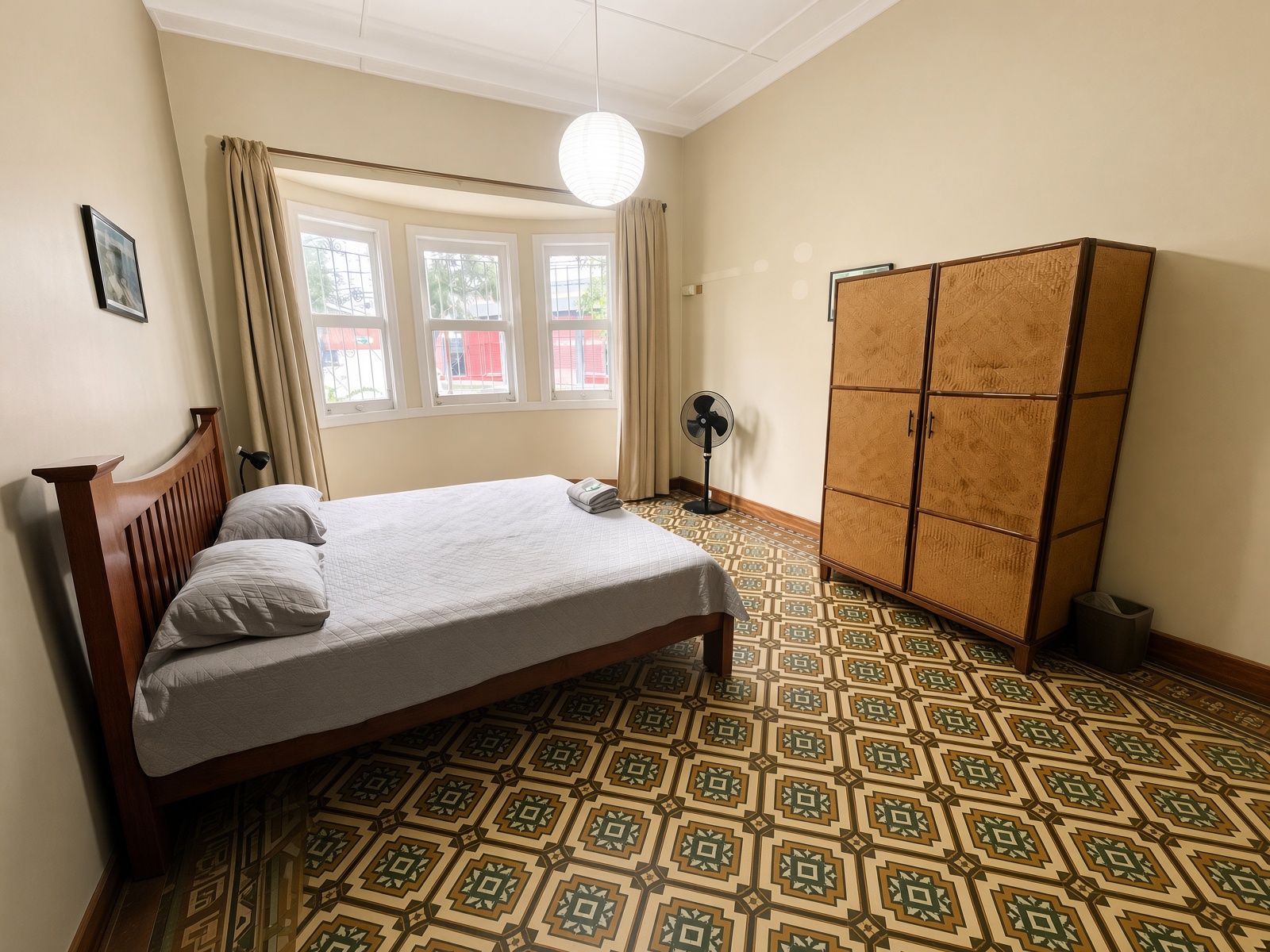 A room with a bed, a wardrobe, a window with curtains, and a patterned floor.