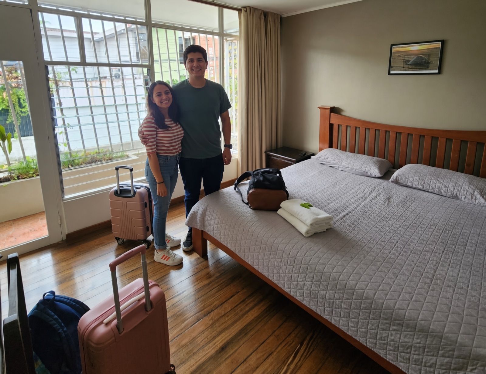 Habitación de hotel con cama, maleta y ventana con vista a edificios.