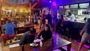 A restaurant with wooden tables and chairs, a bar area, and a kitchen visible in the background.