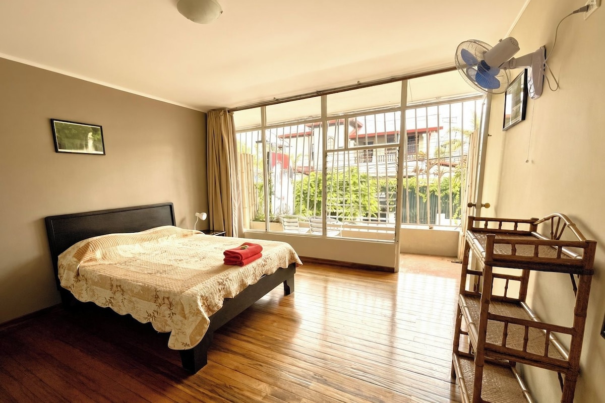 Un dormitorio con una cama, una ventana, un ventilador y un banco de madera.