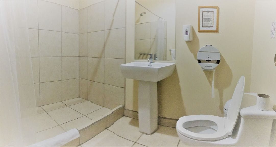 A bathroom with a shower, sink, toilet, and a hand dryer.
