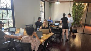 A conference room with wooden tables, laptops, and people working.