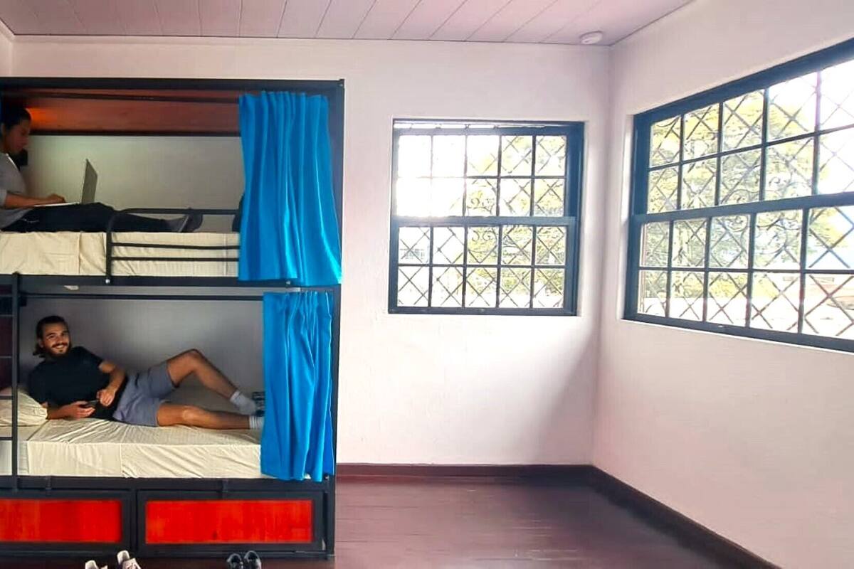 Une chambre avec un lit superposé, une fenêtre avec une grille en métal et une vue sur les arbres à l’extérieur.