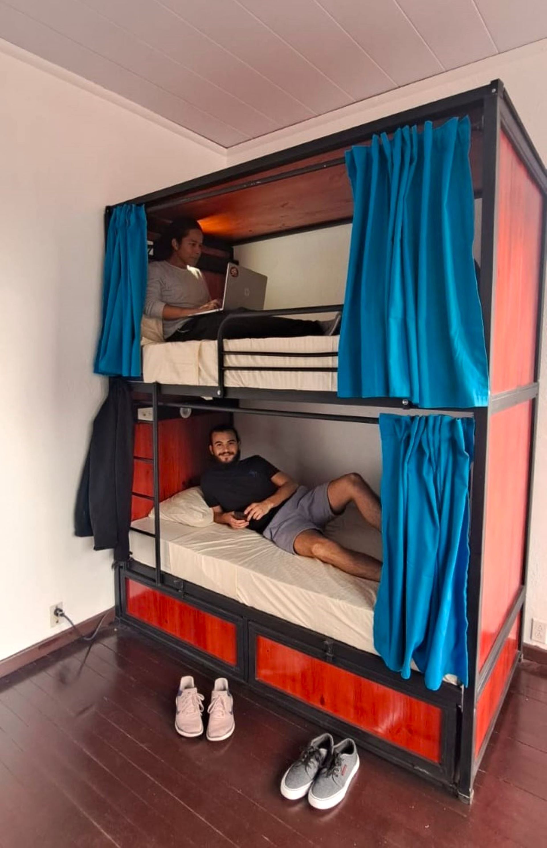 A bunk bed room with two beds, one with a laptop on it, and a pair of shoes on the floor.