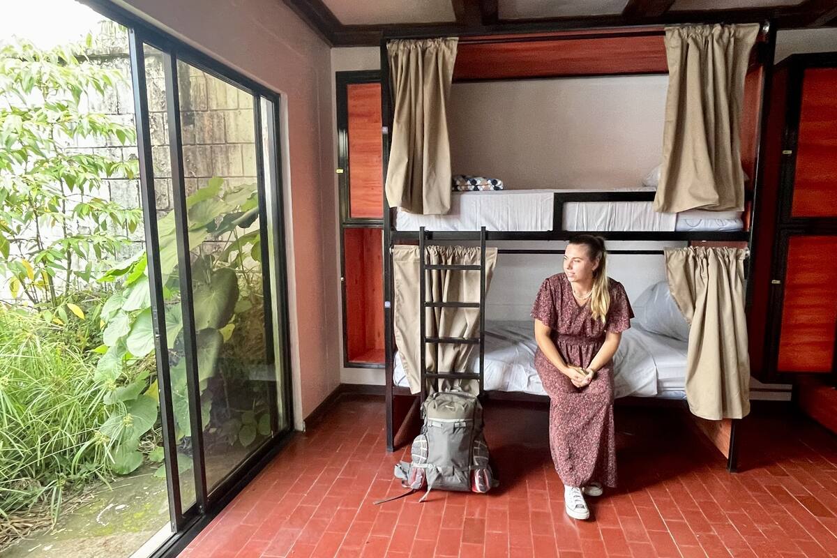 Une chambre avec des lits superposés, une valise et une fenêtre donnant sur un paysage verdoyant.