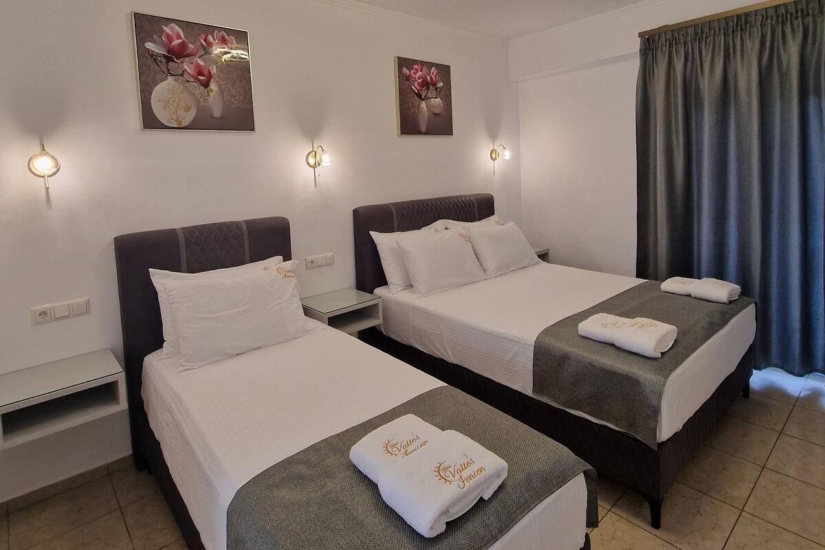 Ein Hotelzimmer mit zwei Betten, einem Flachbildfernseher, einem kleinen Tisch und einer Wandleuchte.