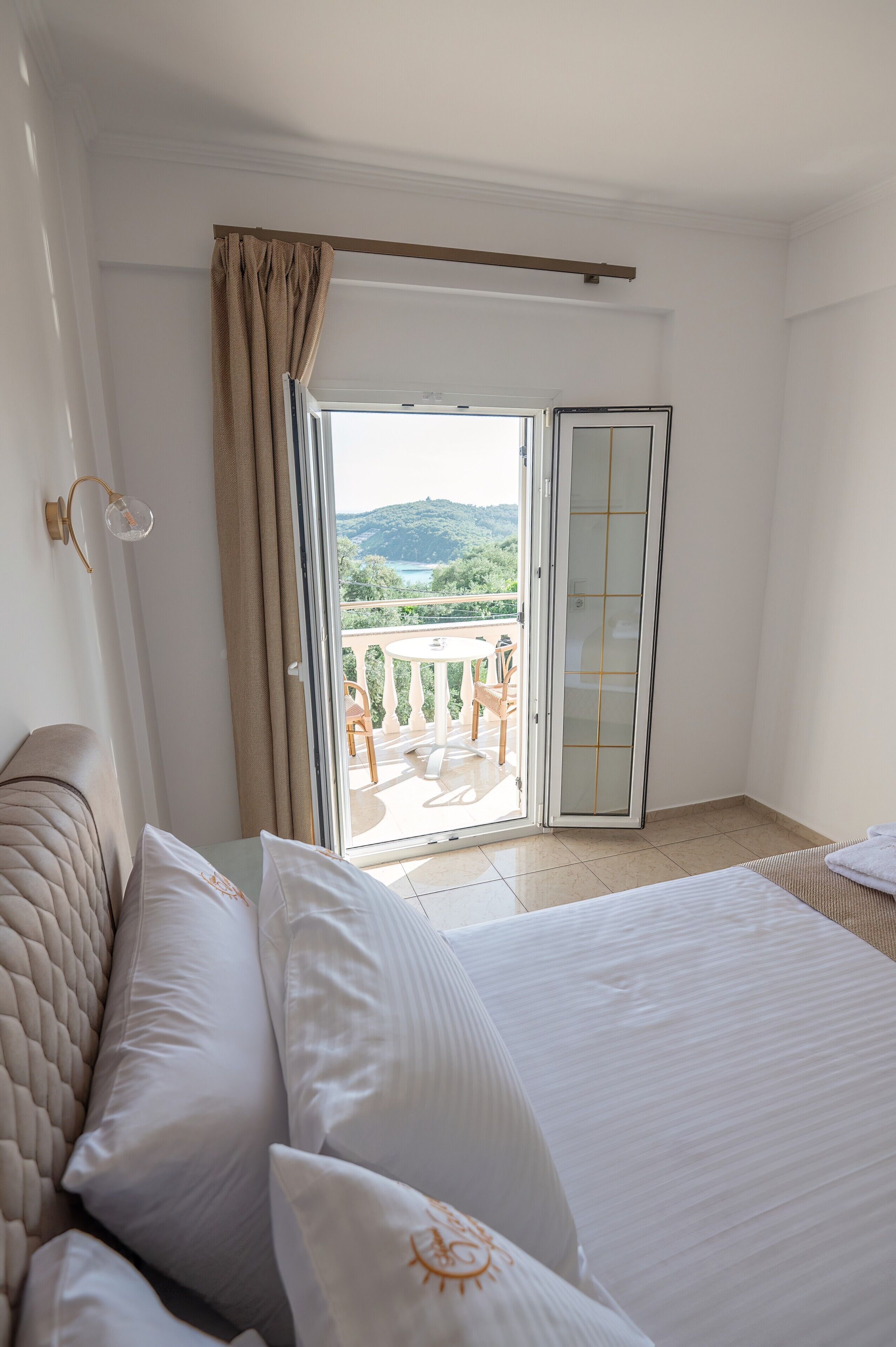 Een hotelkamer met een bed, een balkon met een tafel en stoelen, en een glazen schuifdeur naar het balkon.