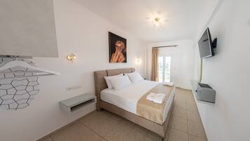 Una camera d'albergo con un letto, una televisione, un televisore a muro, un quadro, una lampada e una finestra.