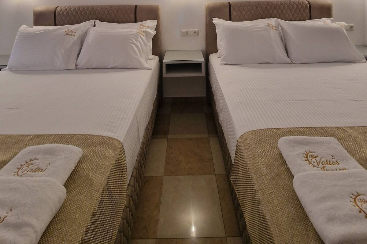 Ein Hotelzimmer mit zwei Betten, einem Nachttisch, einer Wand-Klimaanlage und einem gerahmten Bild über den Betten.