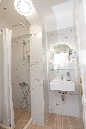 A bathroom with a shower, a glass shelf above the sink, and a marble-patterned wall. - Valtos Ionion (Parga)