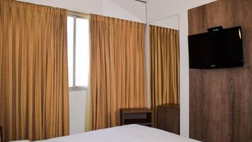 Een hotelkamer met een bed, gordijnen, een televisie en een wand van hout.