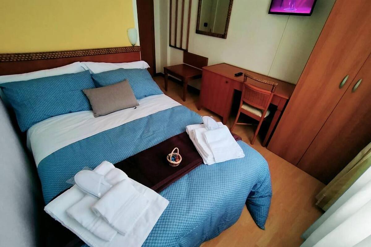 A hotel room with a neatly made bed, a desk, and a wardrobe.