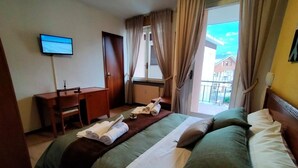 Habitación de hotel con cama, escritorio, televisión y ventana con cortinas.