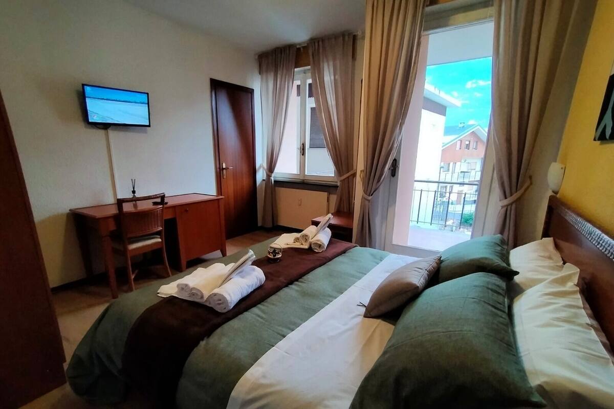 A hotel room with a bed, a desk, a television, and a window with curtains.