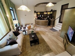 A modern living room with a sofa set, a coffee table, and a TV. There is a kitchen area with a counter and a staircase leading to another level. - Hotel La Chance (Saint-Vincent)