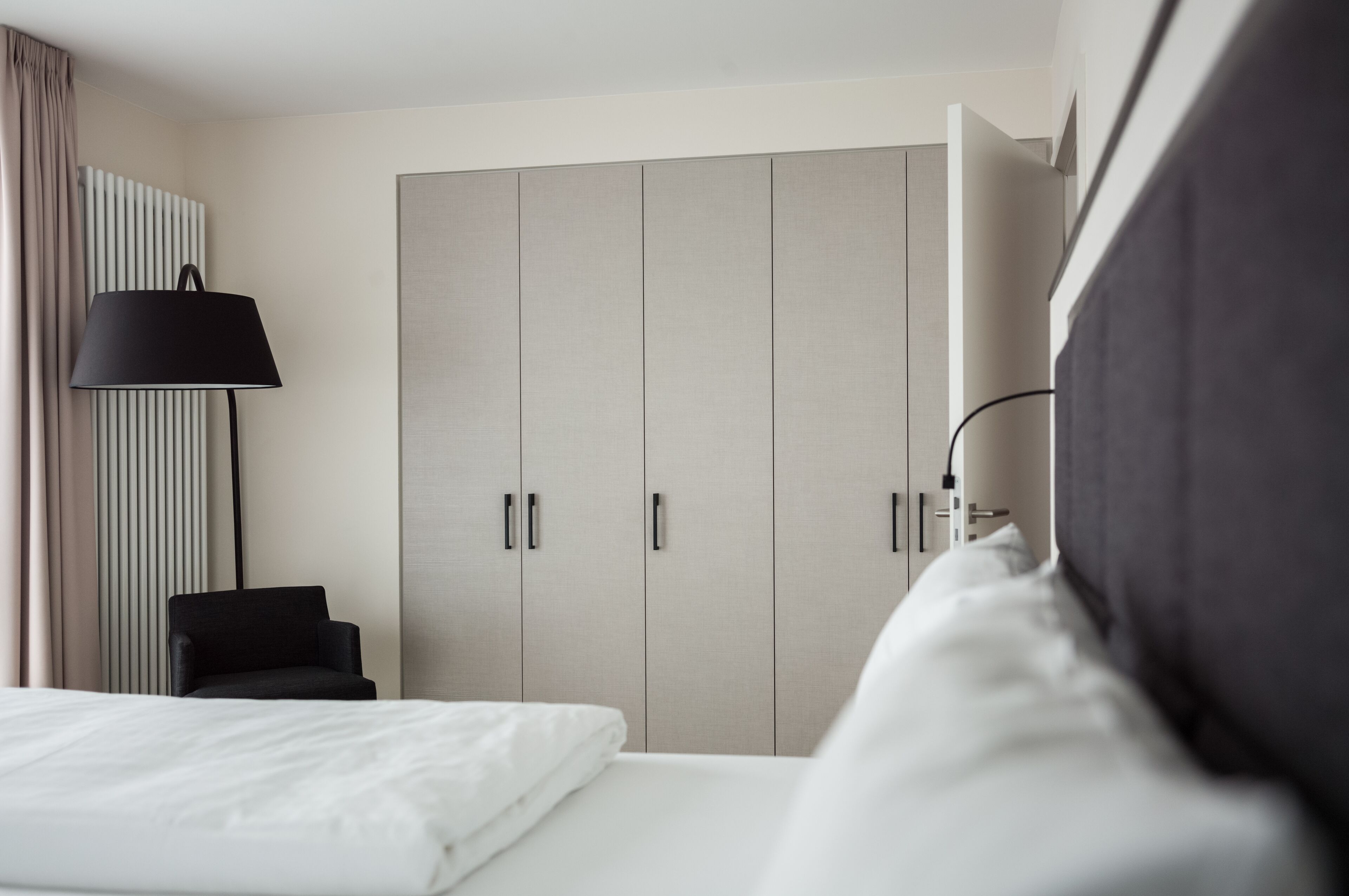 Moderni hotellihuone, jossa on sänky, tuoli, vaatekaappi ja lamppu.