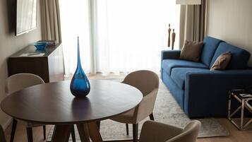 A modern living room with a round wooden table, beige chairs, a blue vase, a blue sofa, and a lamp.