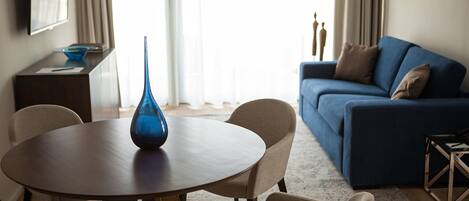 Una sala moderna con una mesa redonda de madera, sillas color beige, un jarrón azul, un sofá azul y una lámpara.