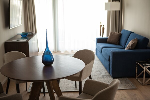 A modern living room with a round wooden table, beige chairs, a blue vase, a blue sofa, and a lamp.